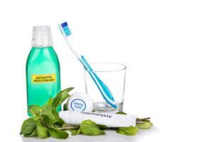 Mouthwash, toothbrush, toothpaste, and floss on a white background surrounded by mint leaves