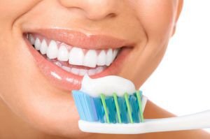 woman smiling with toothbrush and toothpaste by her mouth