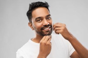 man flossing his teeth against a grey background