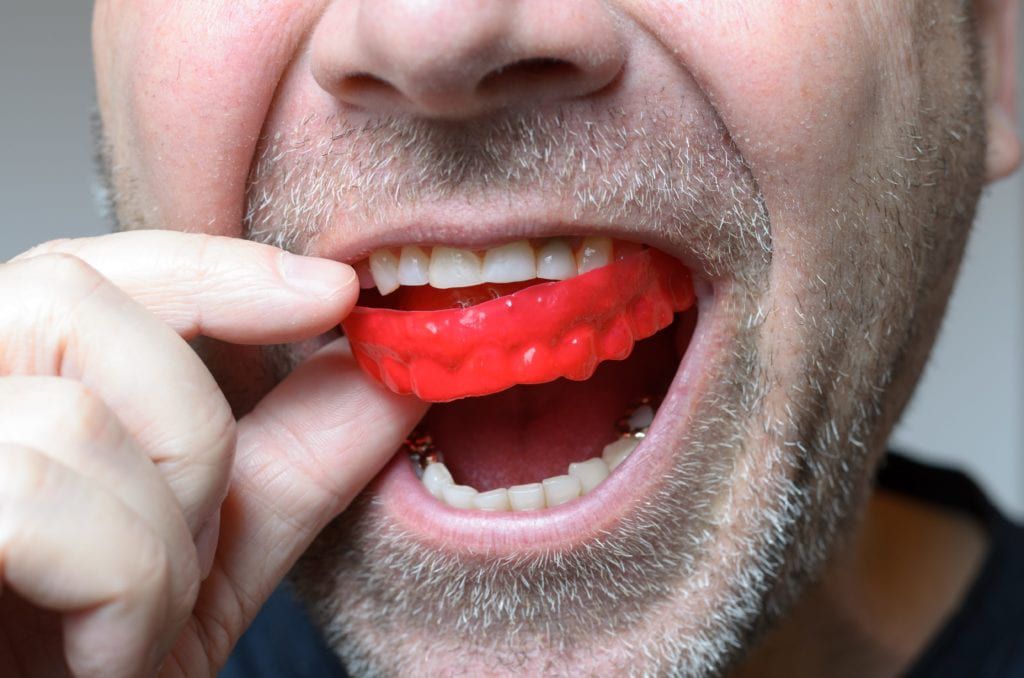 Close up of a man placing a red mouth guard